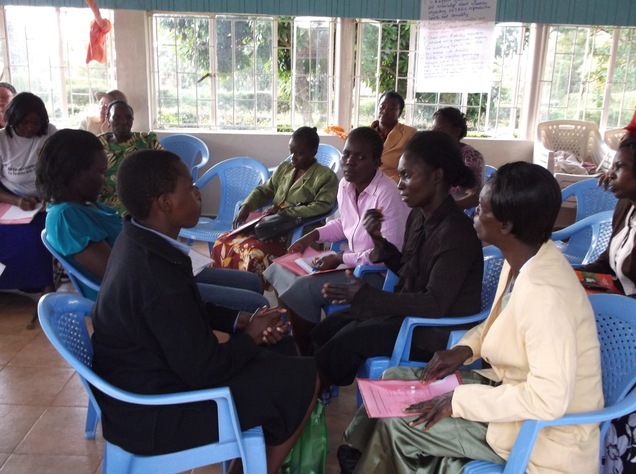 A group of women sitting in plastic chairs have a discussion. One of the women is using sign language.